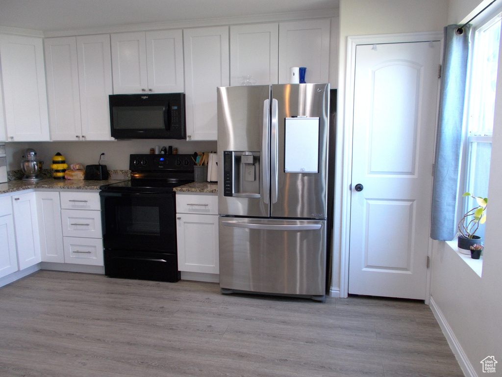 Kitchen with white cabinets, light stone counters, light wood-type flooring, and black appliances