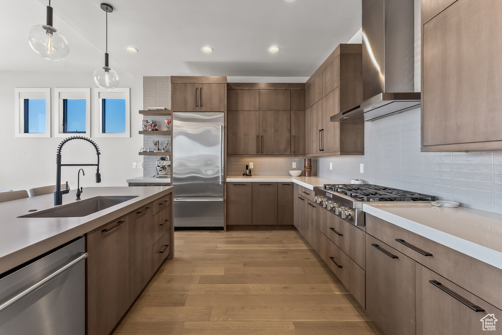Kitchen featuring backsplash, light hardwood / wood-style flooring, sink, appliances with stainless steel finishes, and wall chimney range hood