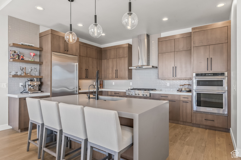 Kitchen featuring appliances with stainless steel finishes, wall chimney range hood, light wood-type flooring, and backsplash