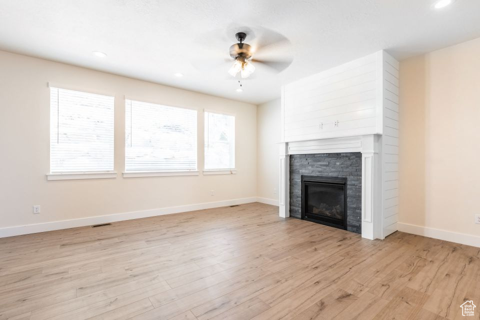 Unfurnished living room featuring a fireplace, ceiling fan, and light wood-type flooring