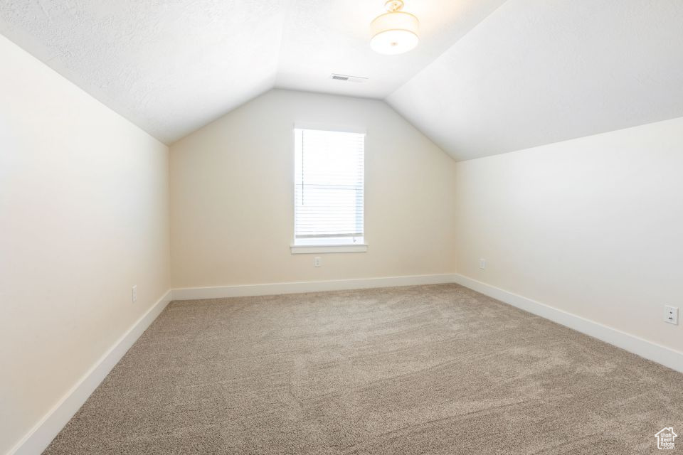Bonus room featuring light colored carpet, vaulted ceiling, and a textured ceiling