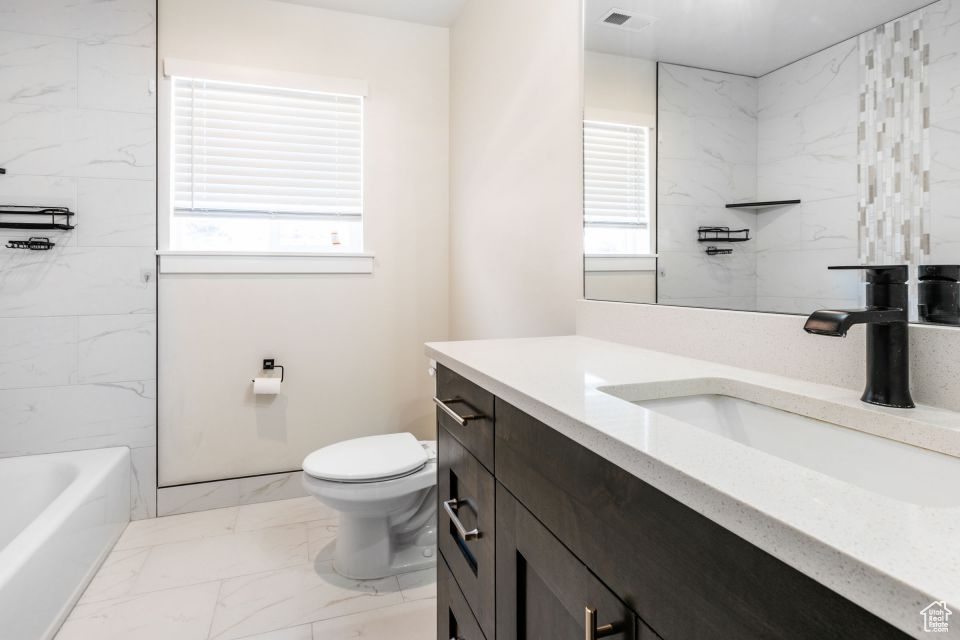 Bathroom featuring vanity with extensive cabinet space, a wealth of natural light, tile flooring, and toilet