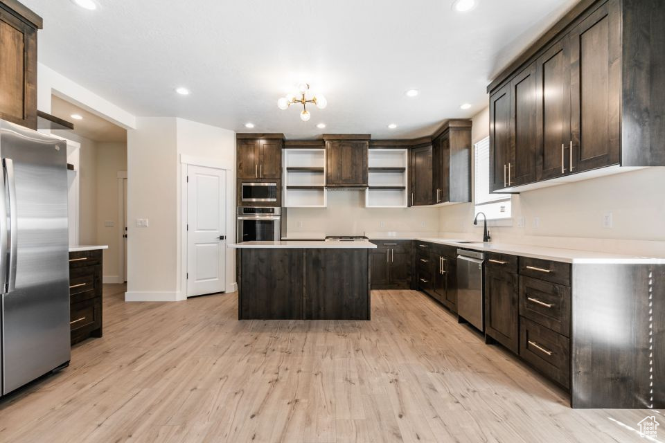 Kitchen with light wood-type flooring, dark brown cabinetry, an inviting chandelier, a kitchen island, and appliances with stainless steel finishes