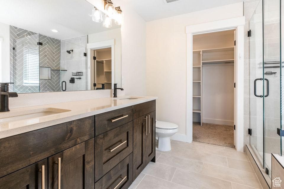 Bathroom with a shower with door, tile flooring, toilet, oversized vanity, and dual sinks