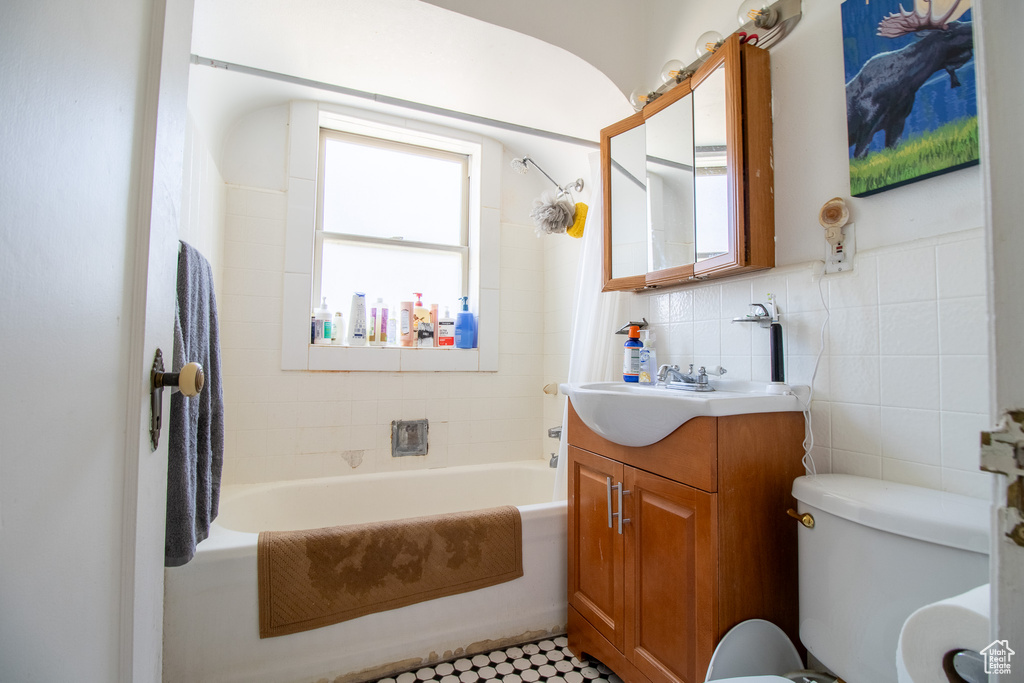 Full bathroom featuring tiled shower / bath, tile walls, tile floors, vanity, and toilet