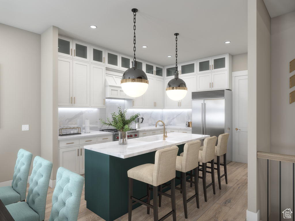 Kitchen featuring light wood-type flooring, a center island with sink, premium range hood, white cabinetry, and backsplash