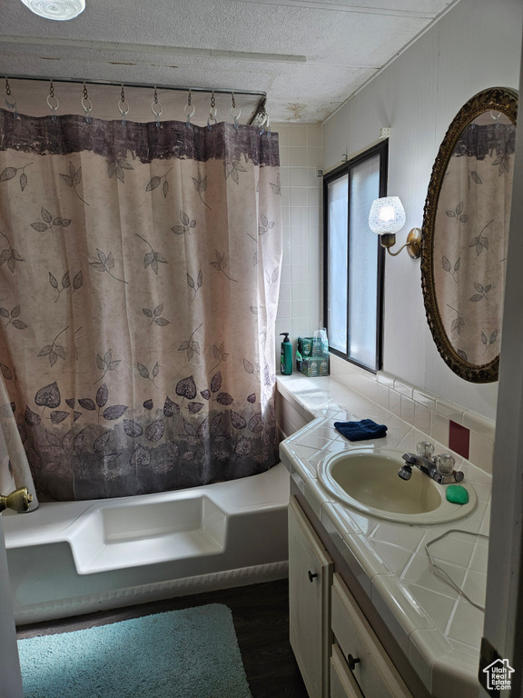 Bathroom with shower / bath combo, hardwood / wood-style floors, large vanity, backsplash, and a textured ceiling