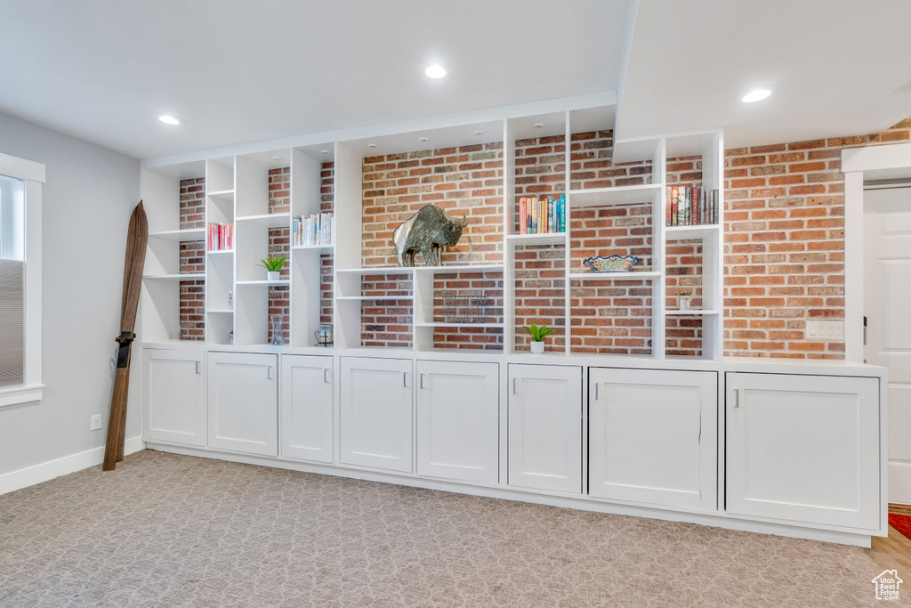 Interior space featuring white cabinetry, light carpet, and brick wall