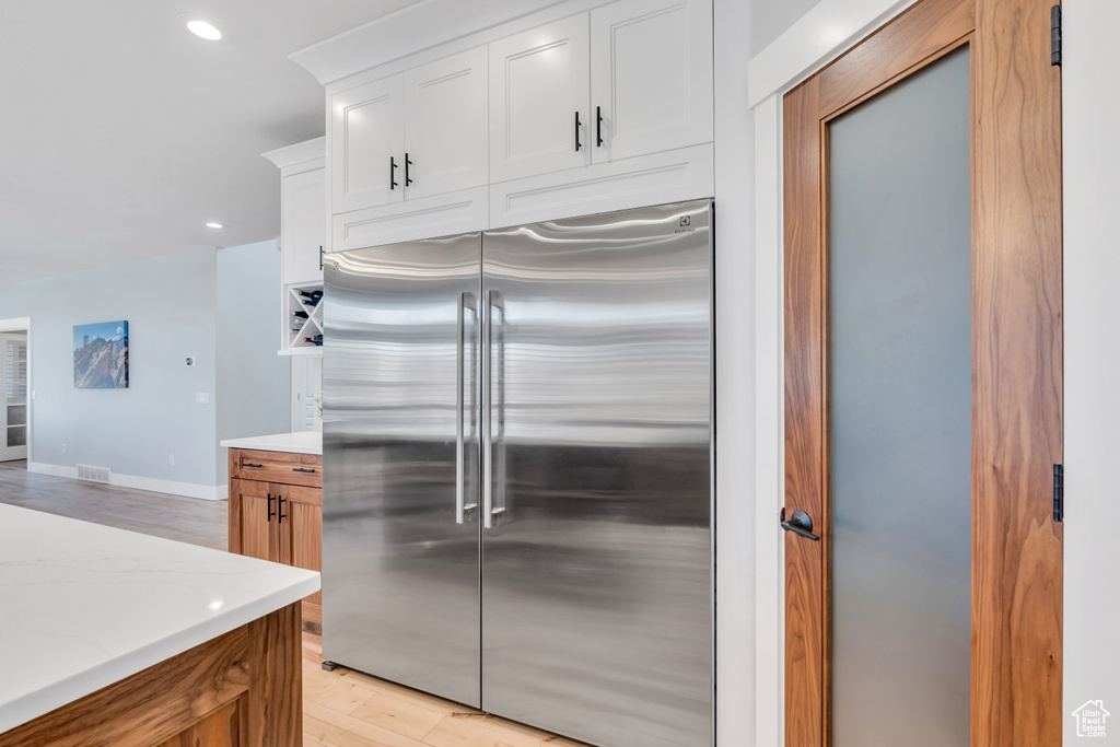 Kitchen featuring white cabinets, light stone counters, stainless steel built in refrigerator, and light hardwood / wood-style flooring