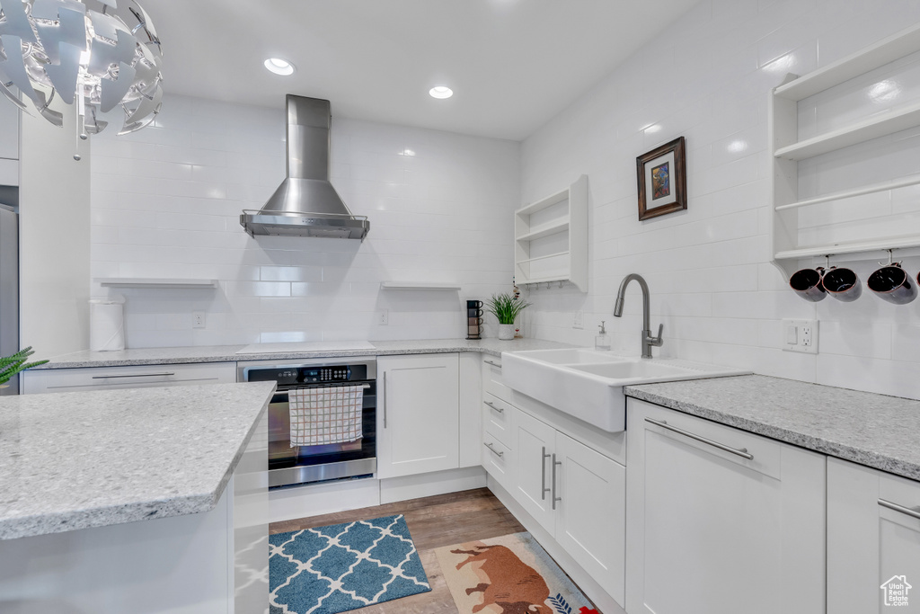 Kitchen with white cabinetry, oven, tasteful backsplash, light hardwood / wood-style floors, and island range hood