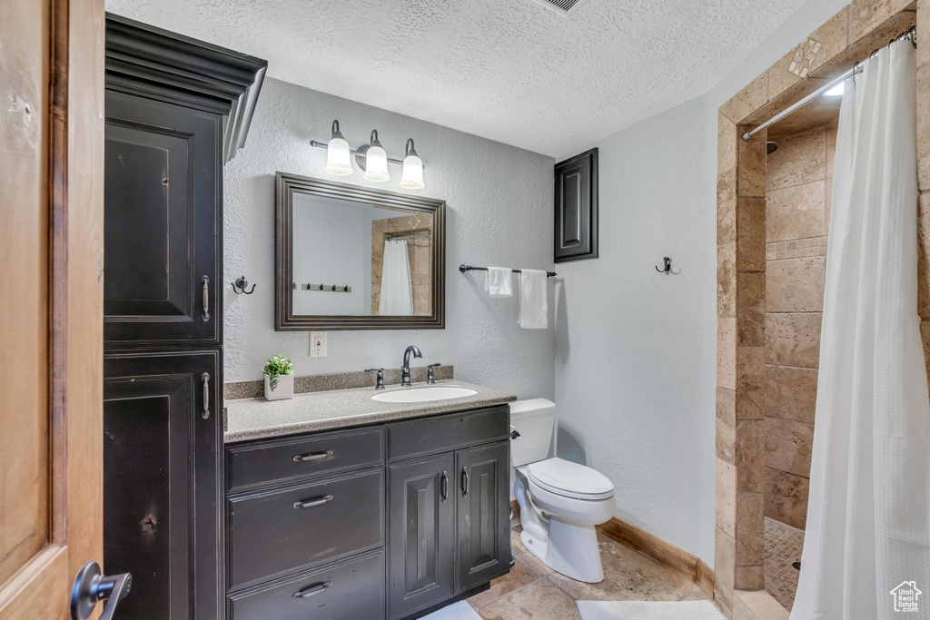 Bathroom with tile floors, a textured ceiling, walk in shower, large vanity, and toilet