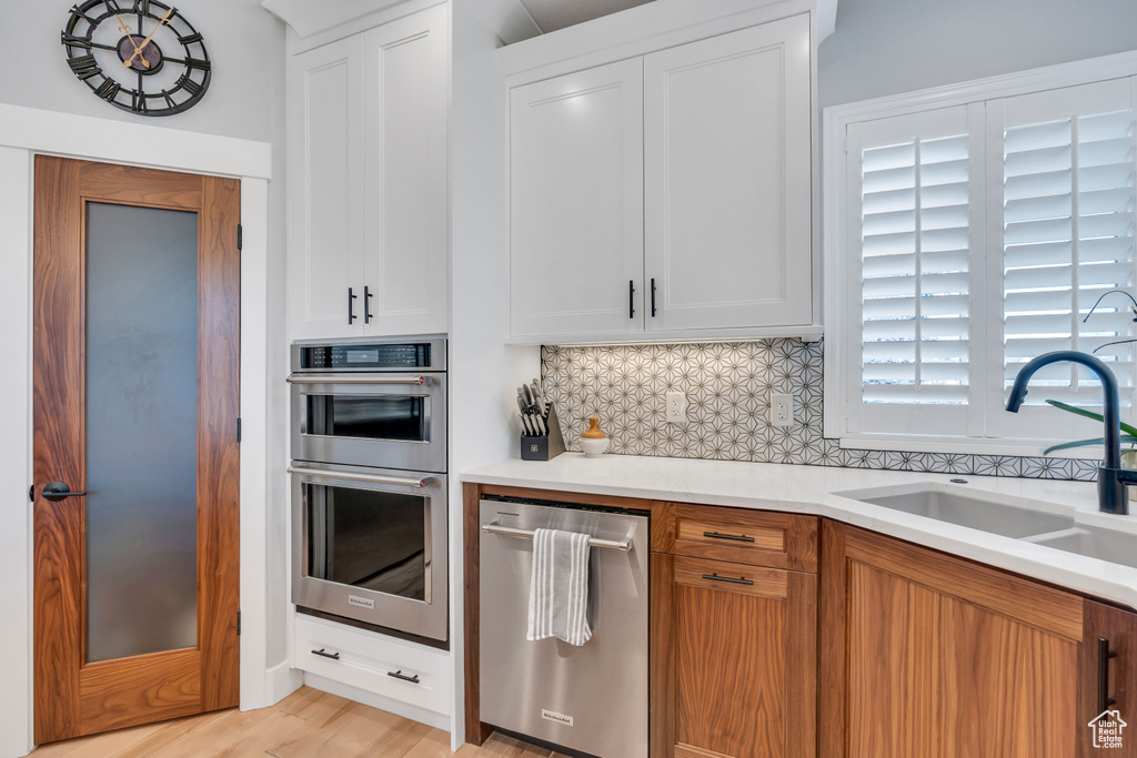 Kitchen with tasteful backsplash, white cabinets, stainless steel appliances, sink, and light wood-type flooring