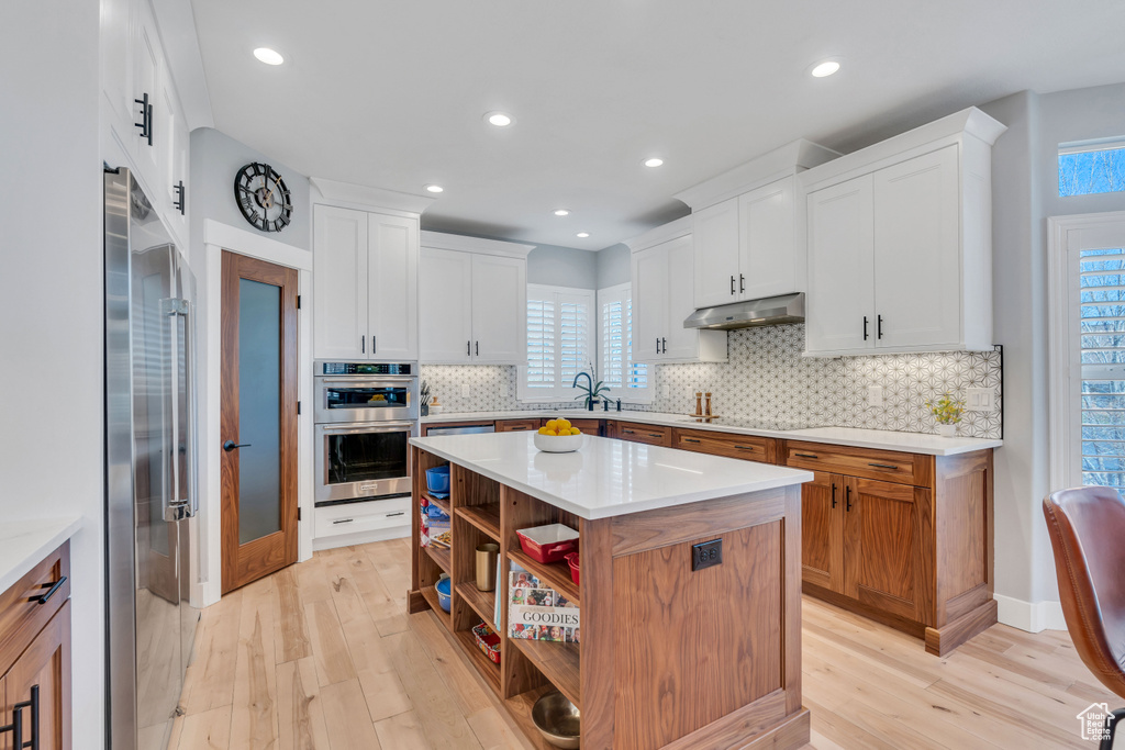Kitchen featuring appliances with stainless steel finishes, white cabinets, backsplash, and light hardwood / wood-style floors