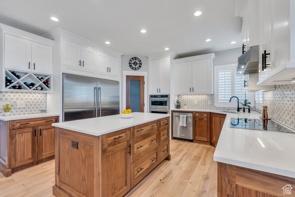 Kitchen featuring a center island, wall chimney range hood, backsplash, light wood-type flooring, and stainless steel appliances