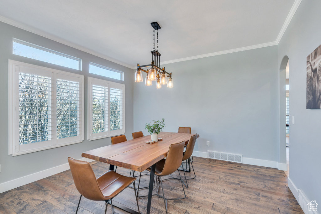 Dining area featuring dark wood-type flooring, a notable chandelier, and crown molding
