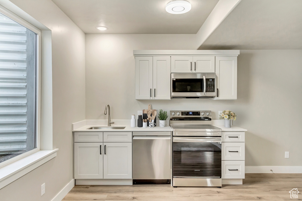 Kitchen with white cabinets, sink, stainless steel appliances, and light wood-type flooring