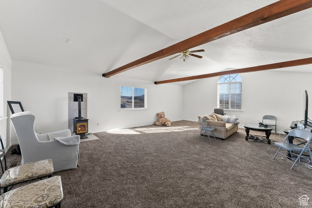 Carpeted living room with vaulted ceiling with beams, a wood stove, and ceiling fan