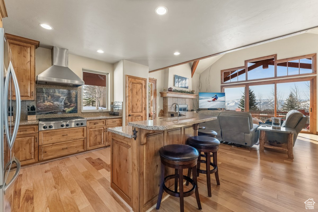 Kitchen featuring light hardwood / wood-style floors, wall chimney range hood, a breakfast bar area, and backsplash
