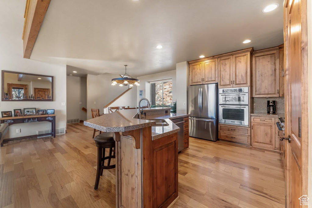 Kitchen with a breakfast bar, stainless steel appliances, sink, a notable chandelier, and light hardwood / wood-style floors