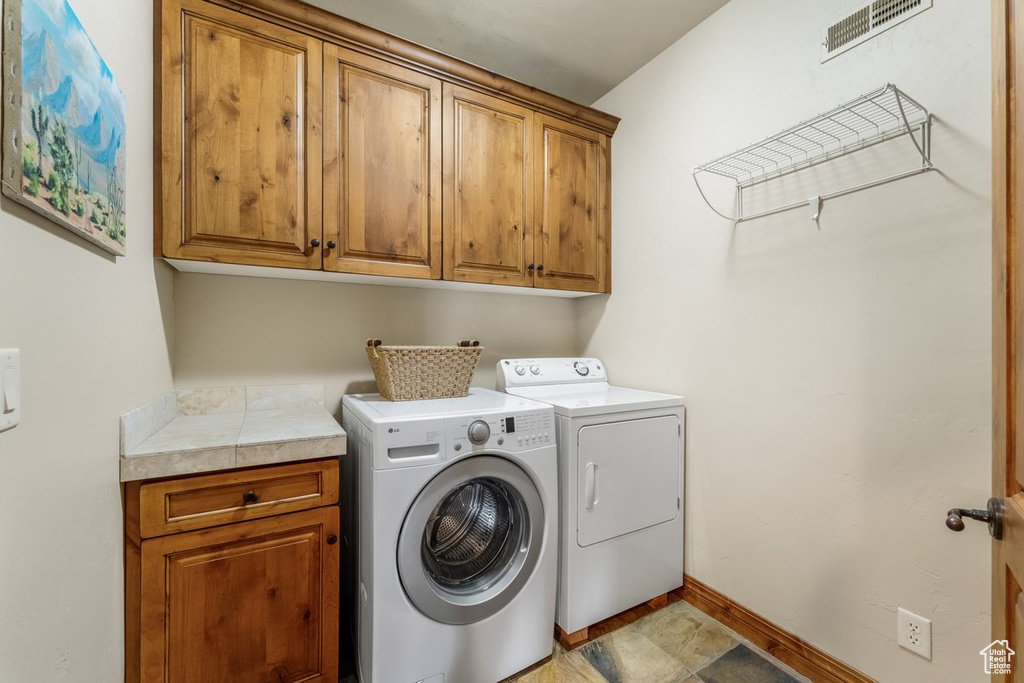 Clothes washing area featuring cabinets, separate washer and dryer, and light tile flooring