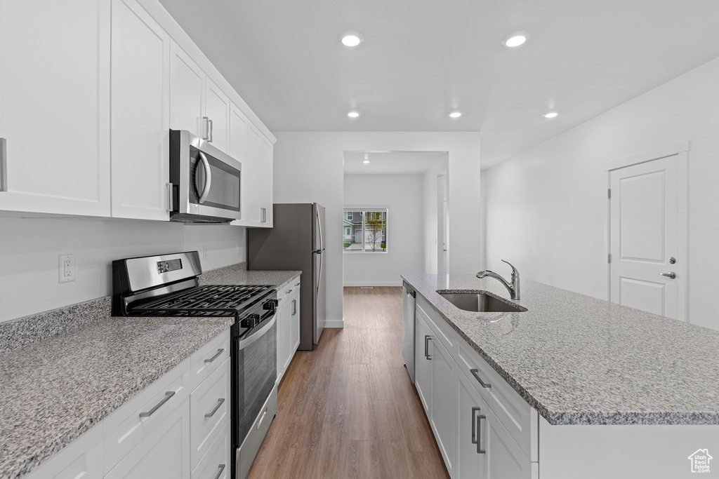 Kitchen with light wood-type flooring, stainless steel appliances, sink, and white cabinetry