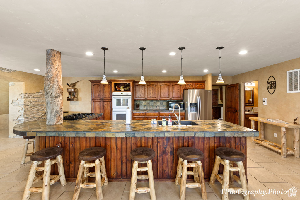 Kitchen with pendant lighting, stainless steel appliances, a kitchen bar, and a kitchen island with sink