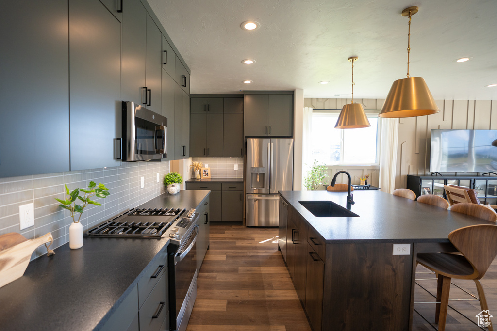 Kitchen featuring pendant lighting, backsplash, sink, appliances with stainless steel finishes, and a kitchen island with sink