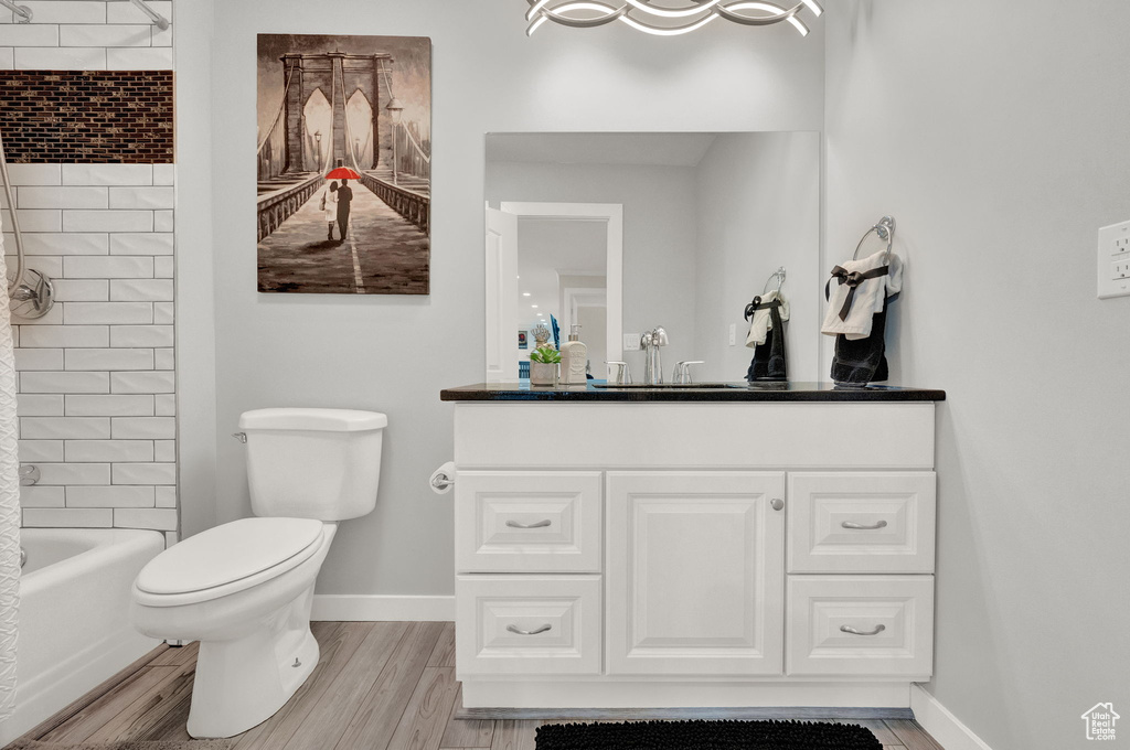 Full bathroom with hardwood / wood-style flooring, tiled shower / bath combo, vanity, and toilet