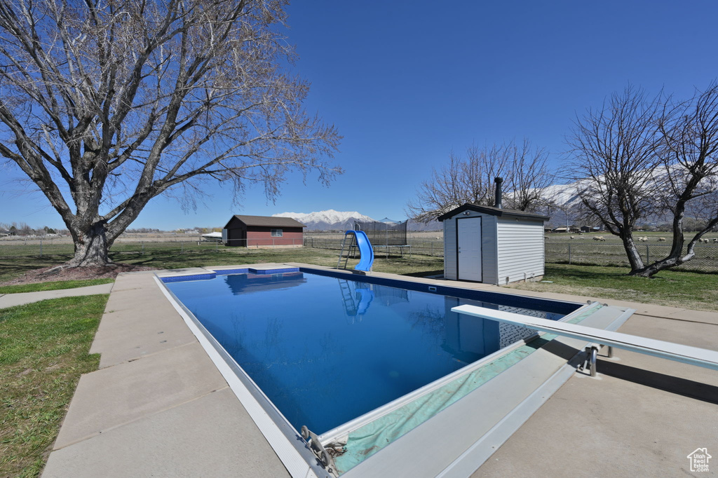 View of swimming pool with a water slide, a yard, a diving board, and a storage unit
