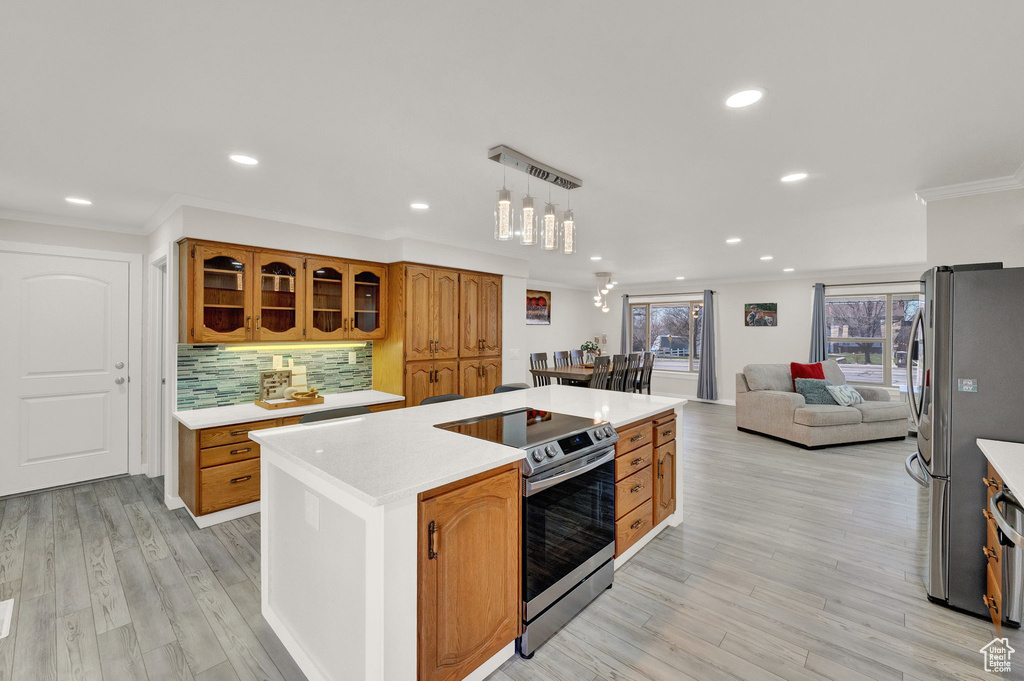 Kitchen with appliances with stainless steel finishes, light wood-type flooring, hanging light fixtures, and tasteful backsplash