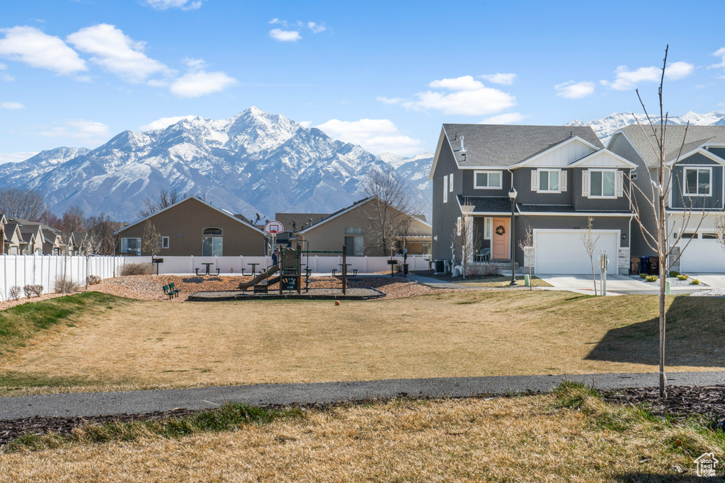 View of front of property with a garage, a mountain view, a front yard, and a playground