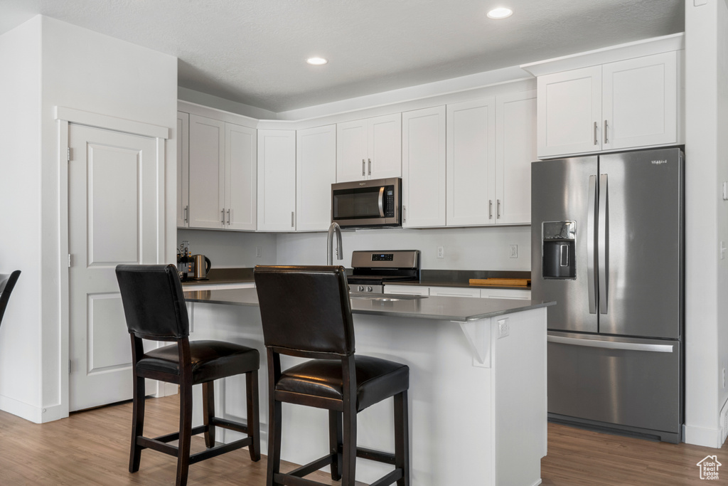 Kitchen featuring a breakfast bar area, stainless steel appliances, a kitchen island, white cabinetry, and hardwood / wood-style flooring