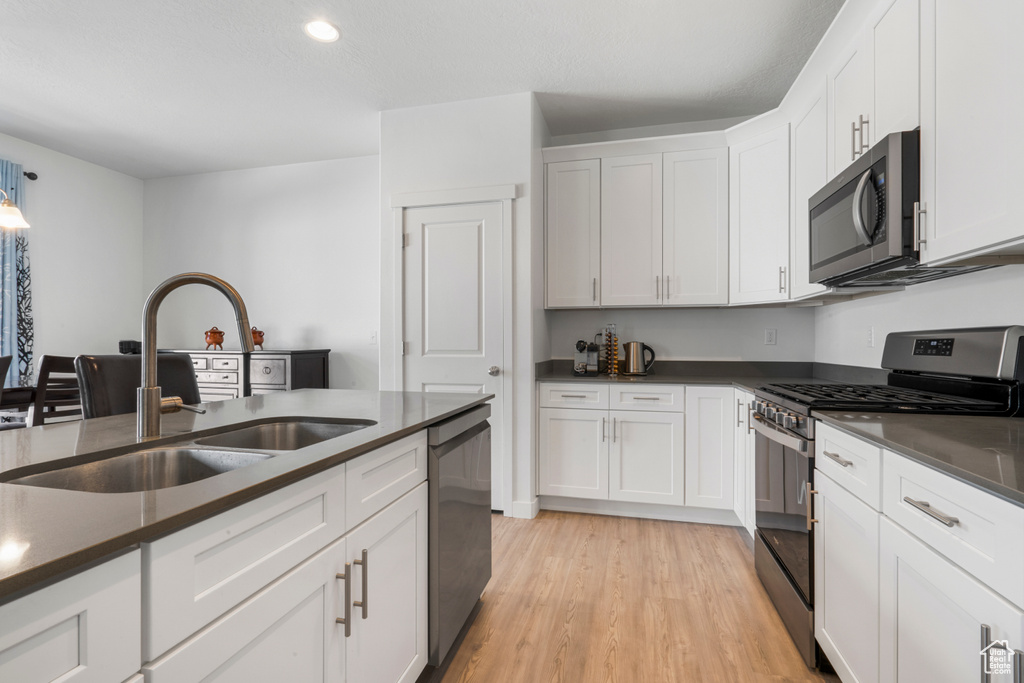 Kitchen with appliances with stainless steel finishes, white cabinetry, sink, and light hardwood / wood-style flooring
