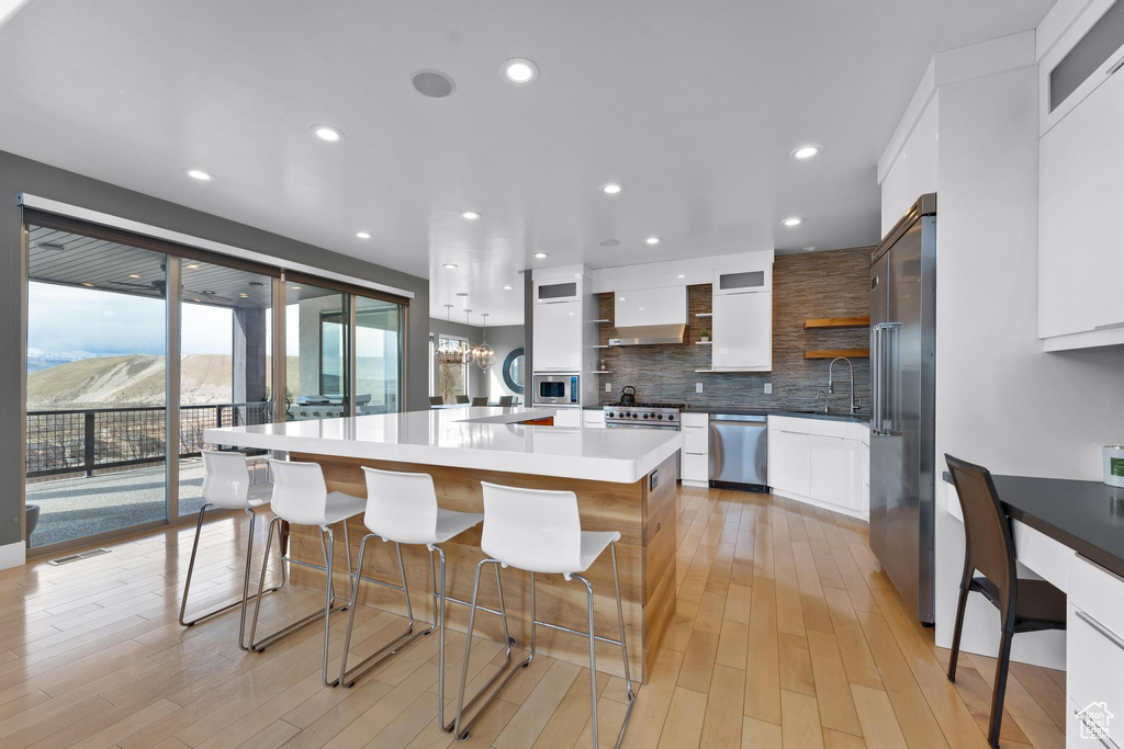 Kitchen with white cabinetry, a center island, a breakfast bar, built in appliances, and backsplash