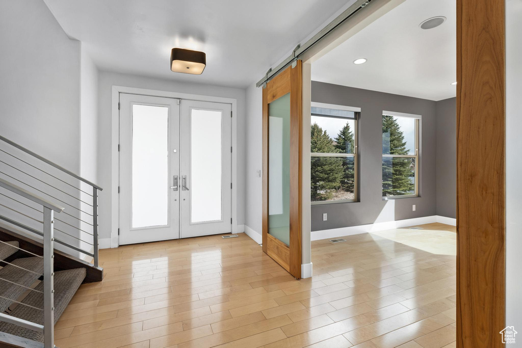 Foyer entrance with a barn door, light hardwood / wood-style floors, and french doors