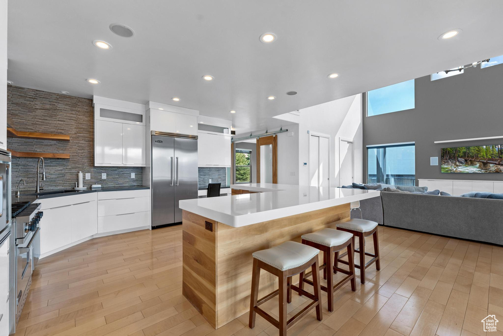 Kitchen featuring white cabinets, light hardwood / wood-style floors, a kitchen bar, stainless steel built in refrigerator, and backsplash