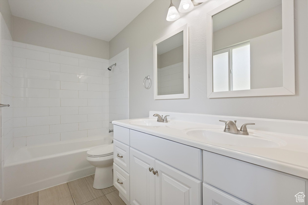 Full bathroom with tile flooring, dual vanity, tiled shower / bath, and toilet