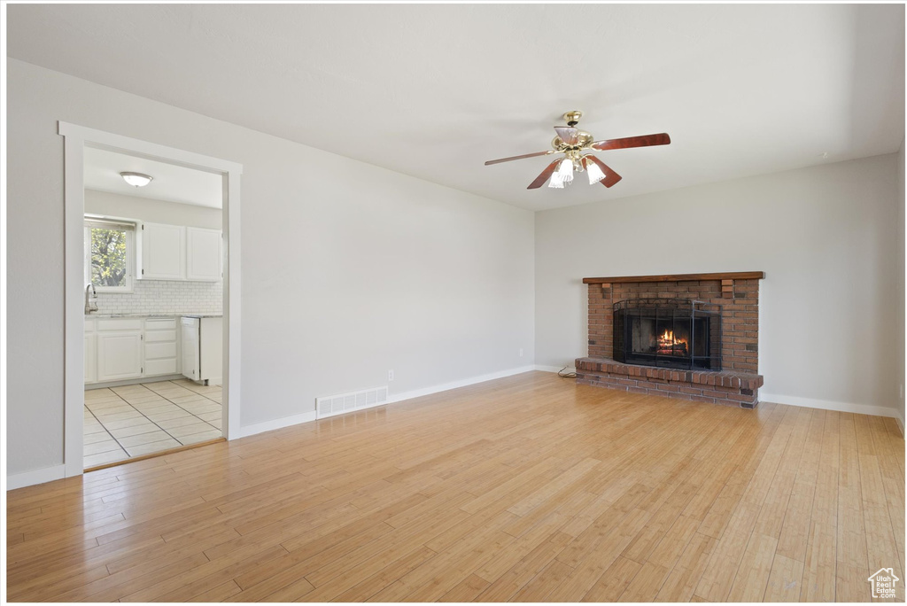 Unfurnished living room featuring light tile flooring, ceiling fan, a brick fireplace, and sink