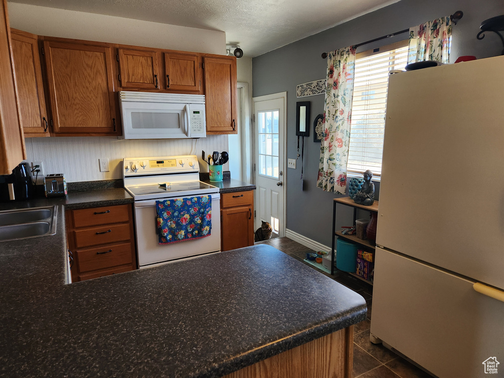 Kitchen featuring plenty of natural light, white appliances, sink, and dark tile floors