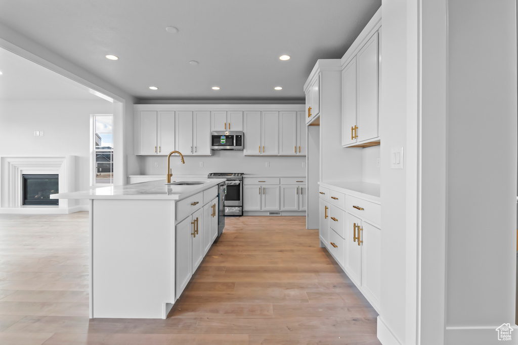 Kitchen with stainless steel appliances, light hardwood / wood-style flooring, white cabinets, a kitchen island with sink, and sink