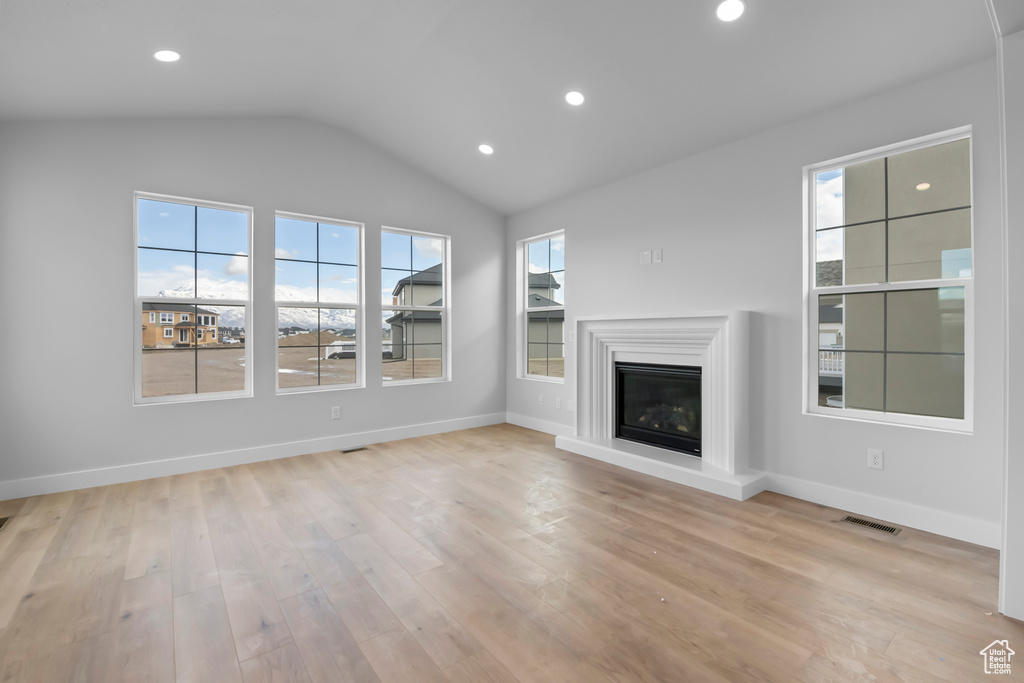Unfurnished living room featuring plenty of natural light, vaulted ceiling, and light hardwood / wood-style flooring