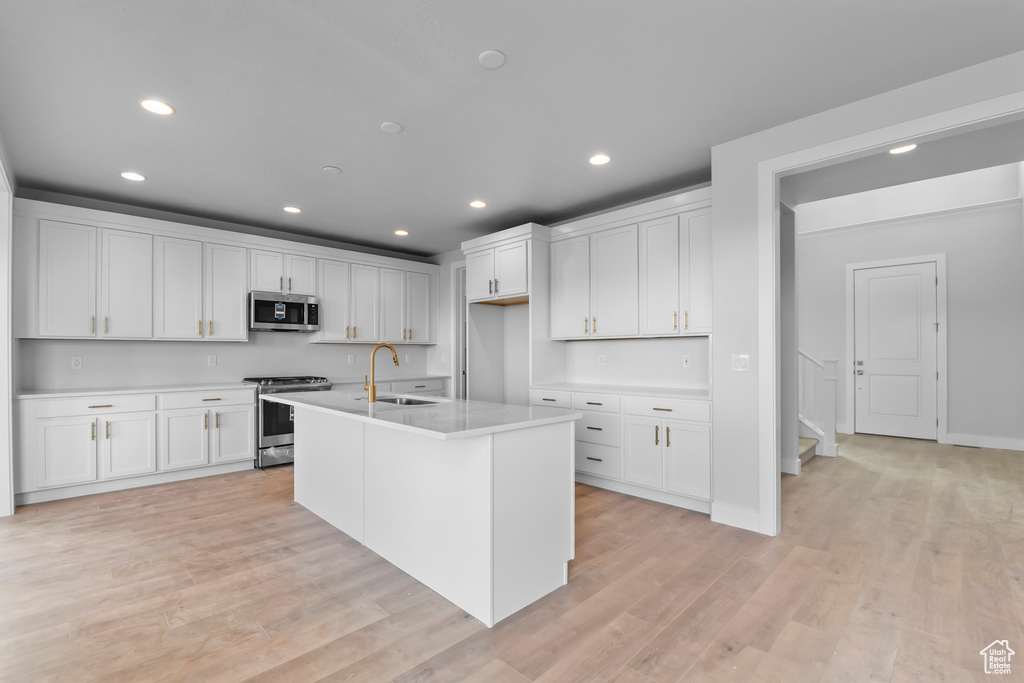 Kitchen featuring white cabinets, appliances with stainless steel finishes, a center island with sink, and light wood-type flooring