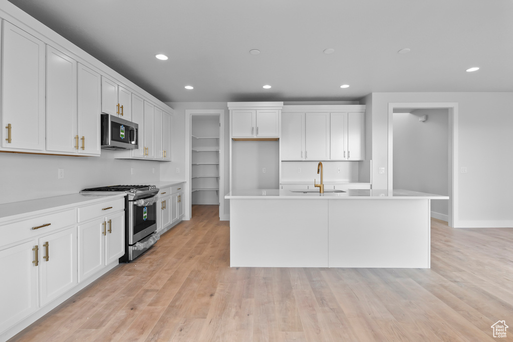 Kitchen with sink, white cabinets, appliances with stainless steel finishes, light hardwood / wood-style flooring, and a center island with sink