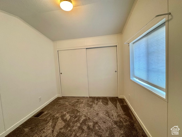 Unfurnished bedroom with dark colored carpet, ornamental molding, and a closet
