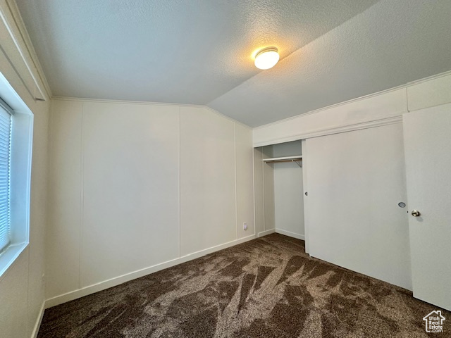 Unfurnished bedroom featuring a closet, dark carpet, a textured ceiling, and vaulted ceiling