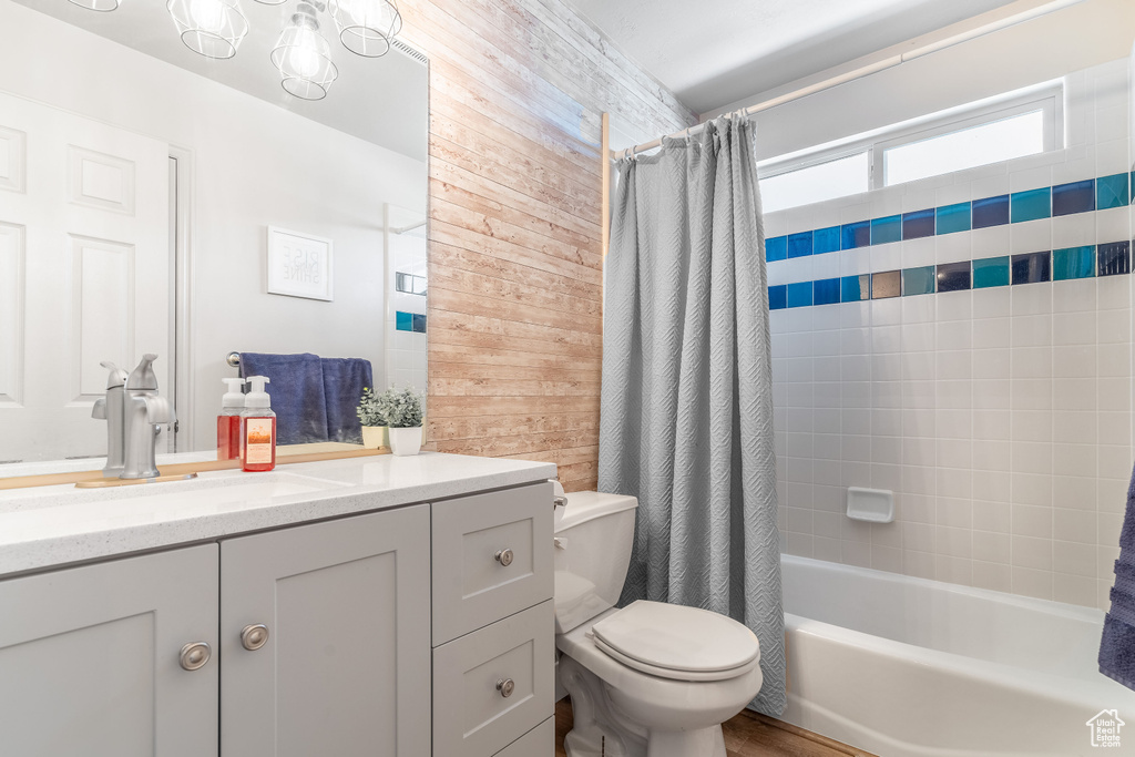 Full bathroom with shower / tub combo, wood walls, vanity, and toilet
