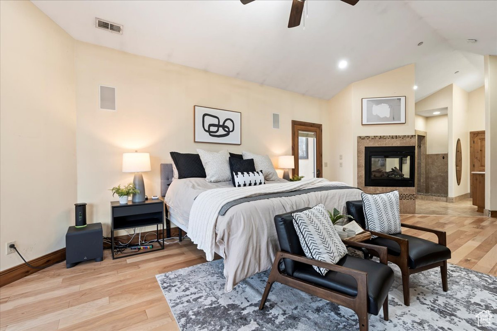 Bedroom featuring light hardwood / wood-style flooring, high vaulted ceiling, a multi sided fireplace, and ceiling fan