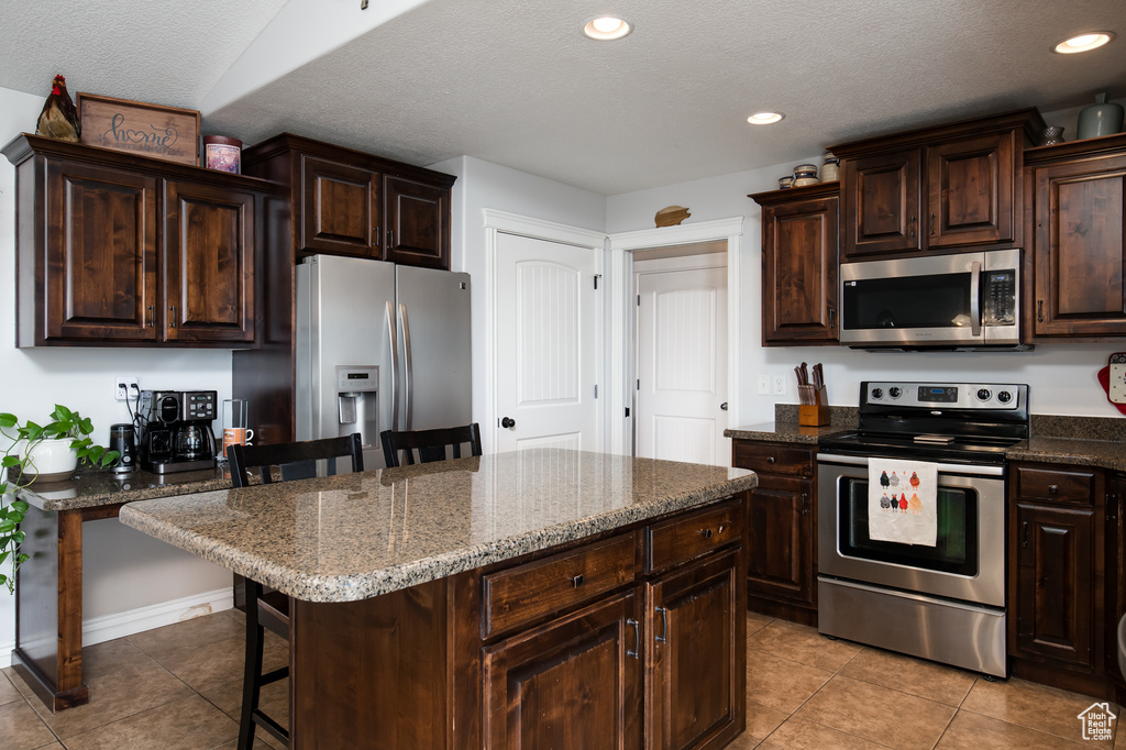 Kitchen featuring a kitchen breakfast bar, stainless steel appliances, light tile floors, and a center island