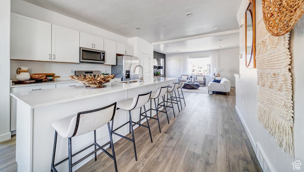 Kitchen with white cabinets, a kitchen breakfast bar, stainless steel appliances, and light wood-type flooring