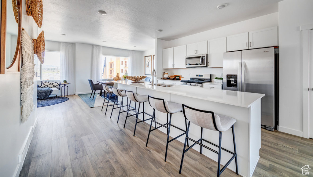 Kitchen featuring a breakfast bar area, stainless steel appliances, light hardwood / wood-style flooring, a center island with sink, and white cabinetry